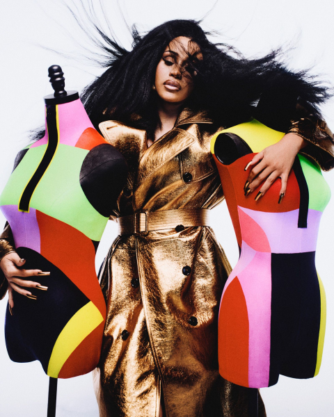 Portrait of Cardi B in gold coat next to two colorful mannequins